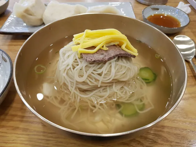 놋그릇에 담긴 평양냉면과 고명으로 얹어진 수육, 계란지단 및 찐만두
