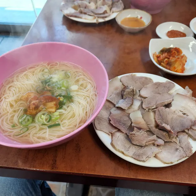 분홍색 그릇에 담긴 멸치국수와 접시에 썰어져 나온 수육