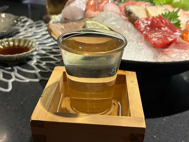 됫잔(마스)에 담긴 유리잔 사케와 그 뒤로 보이는 모둠 사시미