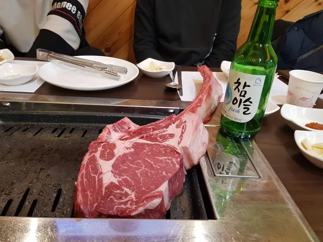 불판 위에 큼직한 토마호크 스테이크 고기와 참이슬 소주병이 놓여 있는 모습