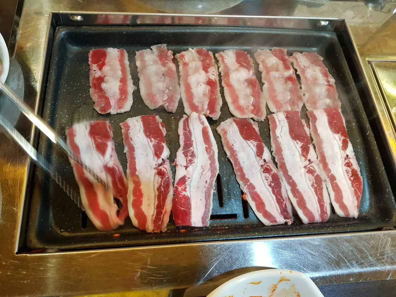 불판 위에 차돌박이 또는 우삼겹을 가지런히 올려 굽는 모습