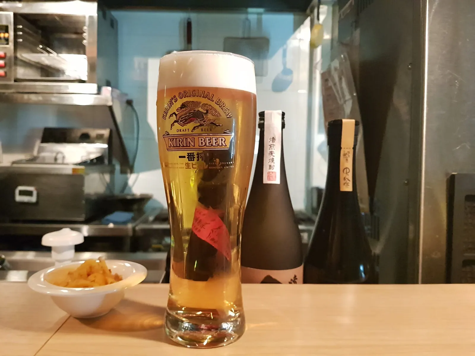 바 테이블 위에 놓인 기린 생맥주 한 잔과 사케 병, 기본 안주