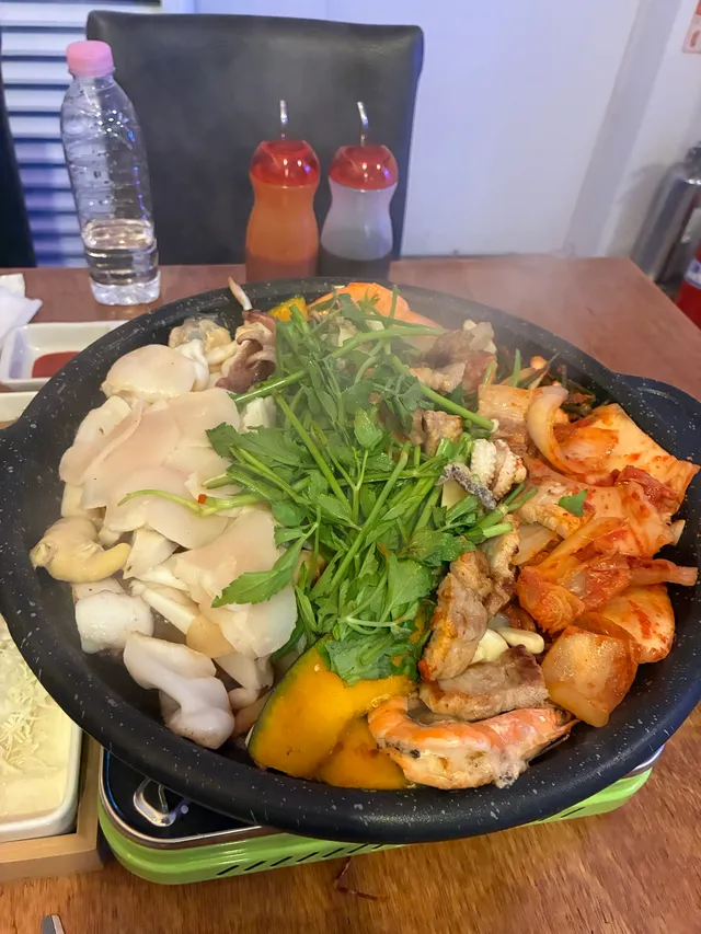 불판 위에 관자, 삼겹살, 김치, 미나리, 단호박, 새우 등이 푸짐하게 올라간 해물삼합 구이
