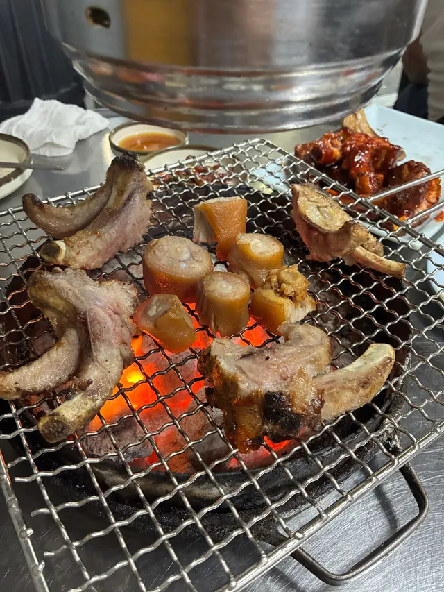 숯불 화로 석쇠 위에 쪽갈비와 돼지꼬리 구이가 구워지고 있는 모습