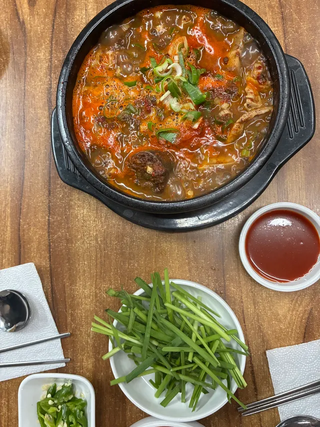 뚝배기에 끓고 있는 얼큰한 순대국과 부추, 청양고추, 양념장이 차려진 테이블